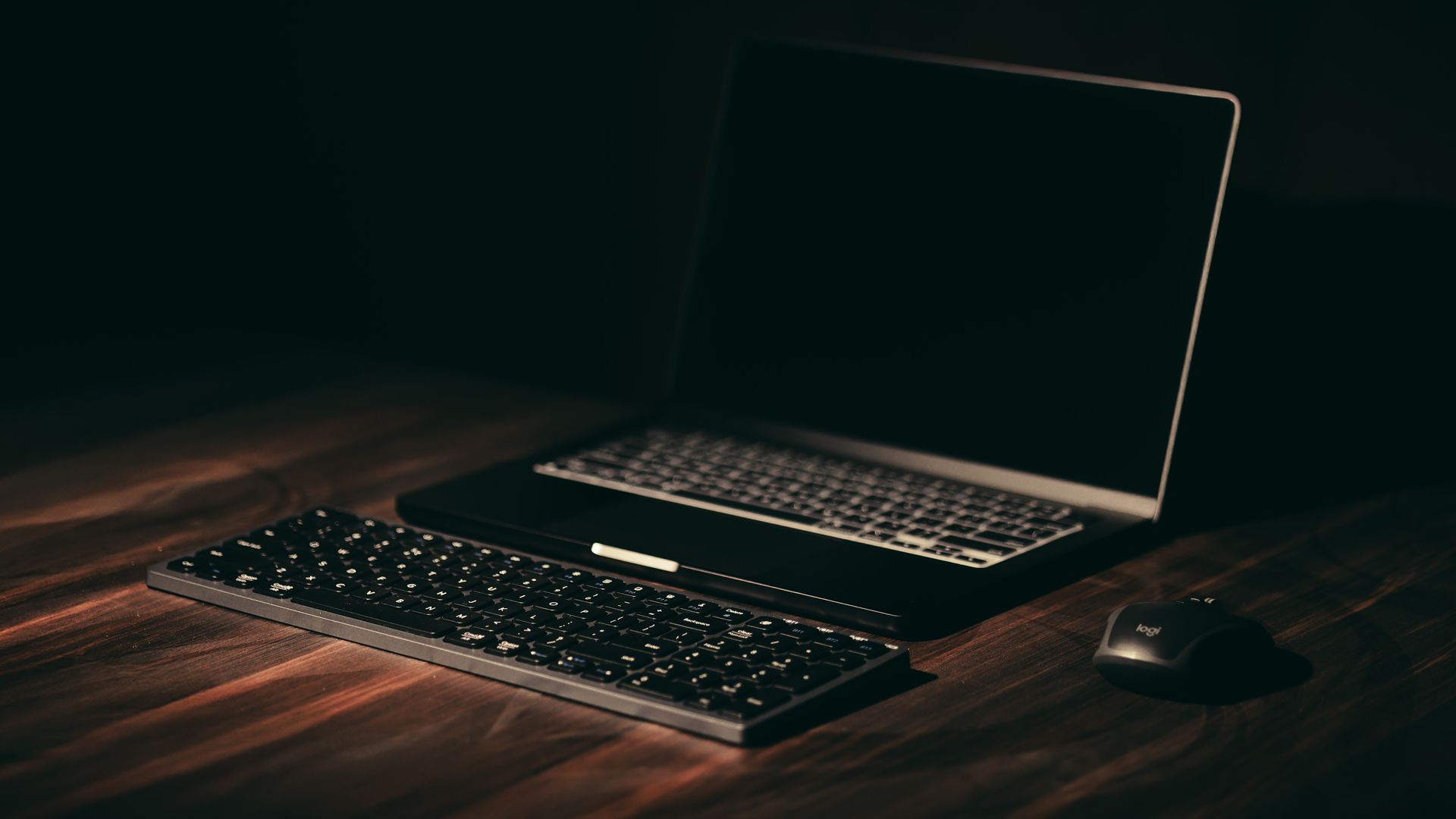 A laptop, keyboard and mouse on a wooden desk in moody light — a developer workspace