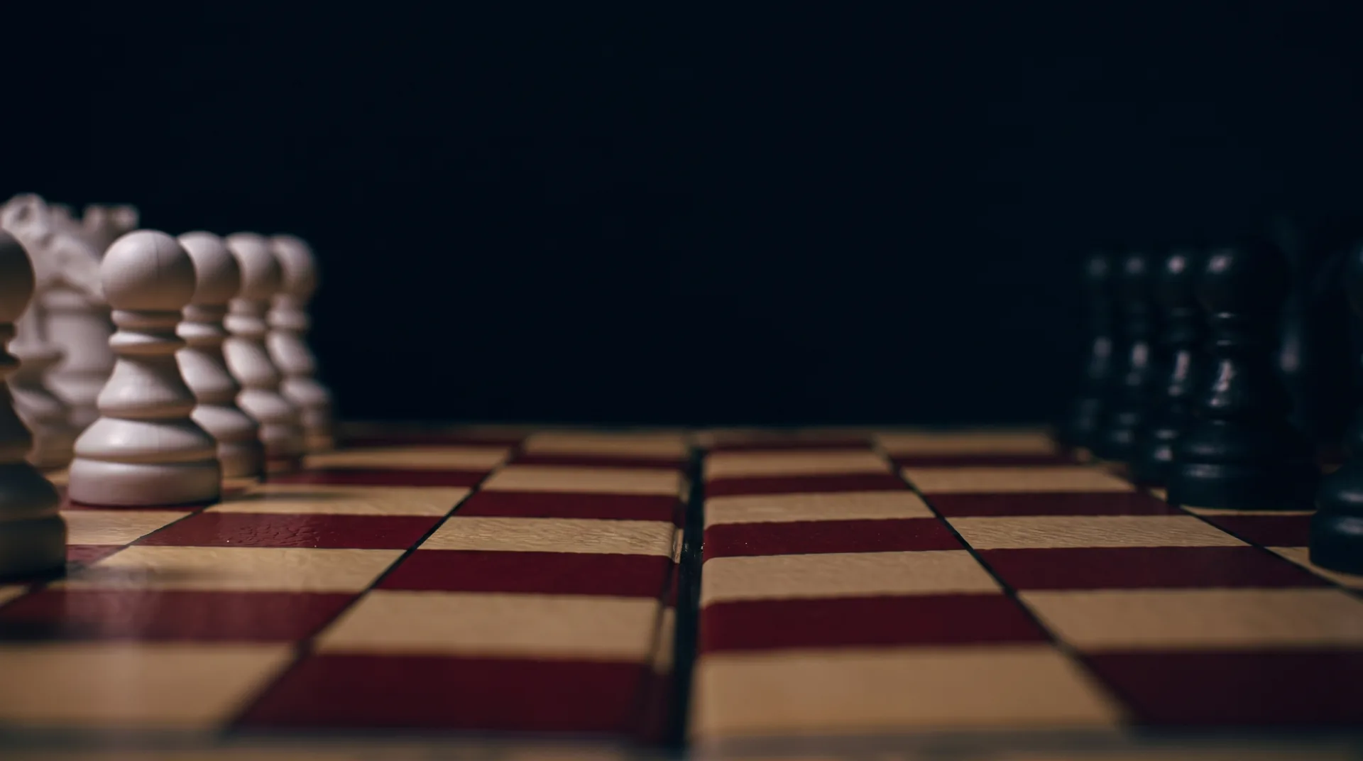 Wooden chess pieces lined up on a red-and-cream board in dramatic low light — strategy and ranking
